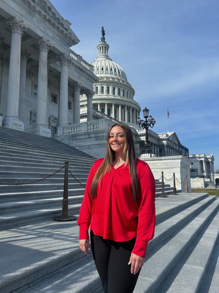 A young woman in red stands on the steps outside Congress.