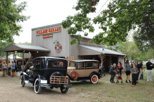 People gather around antique cars at an old garage.