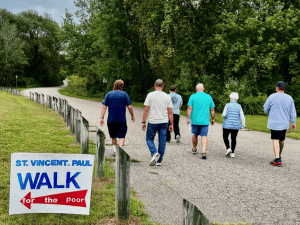 A group of people walk on a country road near some trees.
