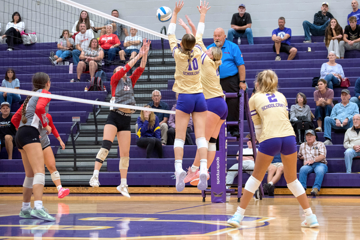 Girls in purple and gold uniforms jump to hit the volleyball back over the net.
