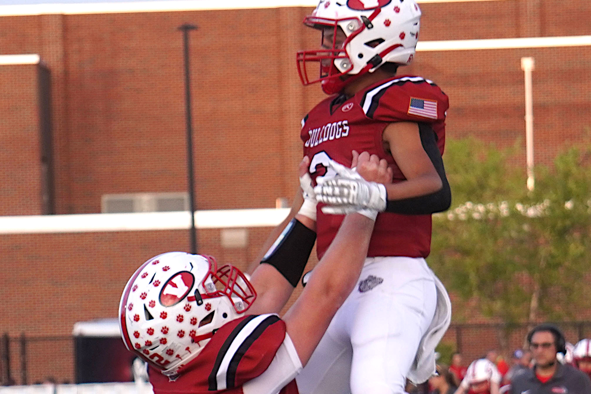 A red uniformed football player lifts a teammate up in the air.