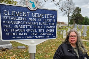 A woman stands near a cemetery marker.