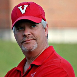 A man with a gray goatee and a red baseball cap and shirt.