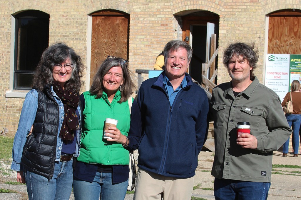 Four people stand near an old brick building.