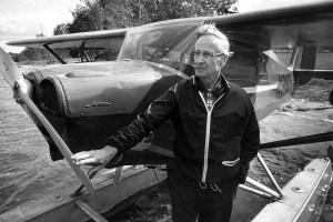 A man stands near a small aircraft in a black and white photo from 1960.