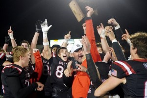 Football players in black, red, and white uniforms hold a trophy high above their heads.