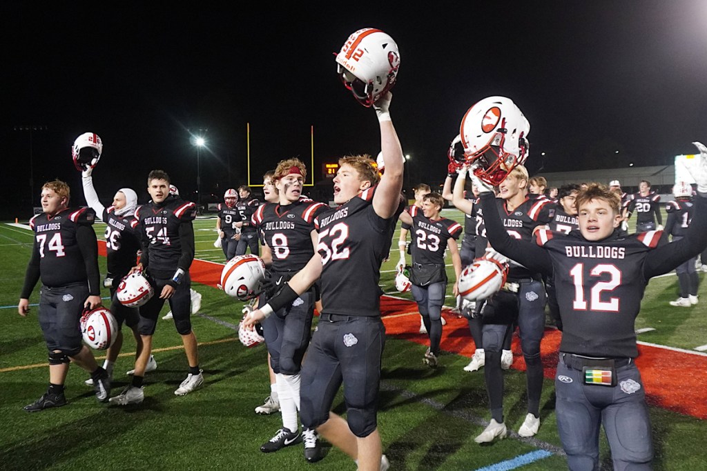 Football players hold their helmets up, celebrating a win.
