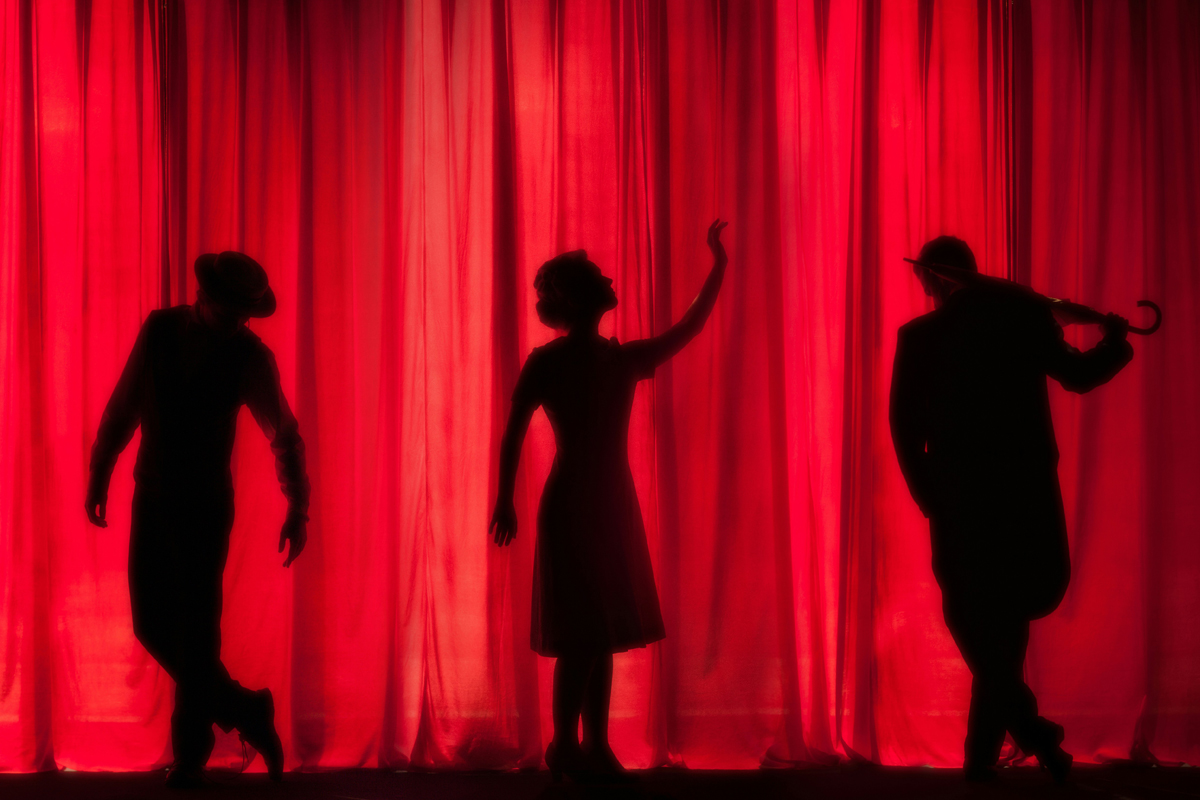 schoolcraft_dramachoir Three shadowy performers behind a red stage curtain.