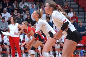 Three volleyball players watch intently.