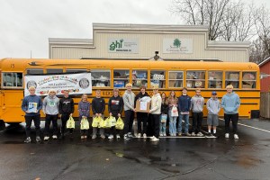 Students line up in front of a yellow school bus with bags of donated food.