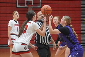 Two basketball players await the tipoff while a referee holds the ball.