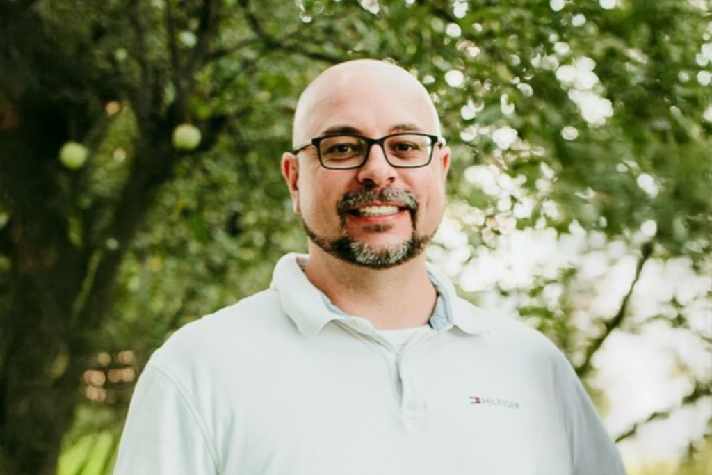 A man with a beard and glasses in a white collared shirt.