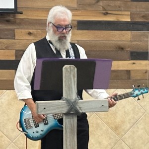 David Thomas holds a guitar, standing at a church altar.