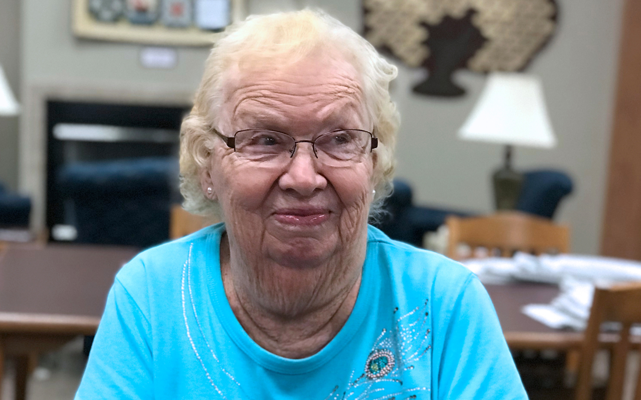 cover_marilyn A senior woman sits with her arms folded, wearing glasses and a bright blue t-shirt.