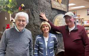 Three people stand near a fake tree inside a library building.