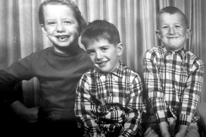 A vintage black and white photograph of the young Oswalt siblings, a girl and two boys in flannel.