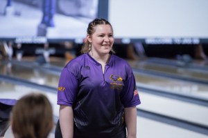 A bowler in a purple jersey stands by the lanes.