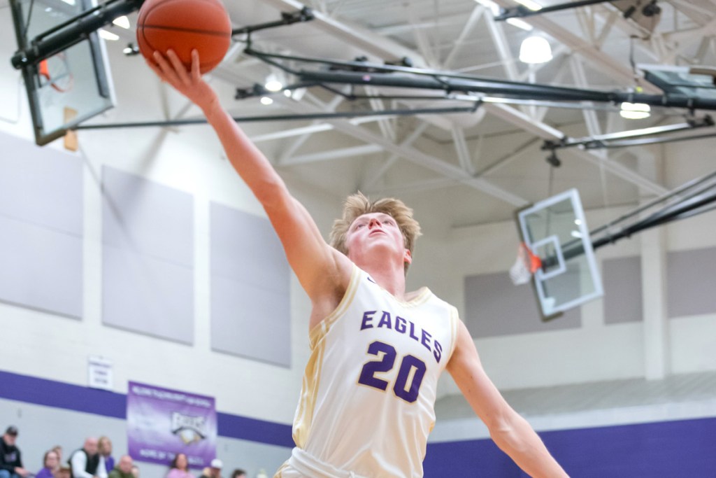 A basketball player in white and purple leaps up with the ball to score.