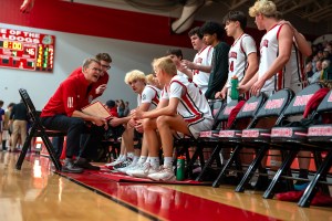 Coaches have an intense discussion with several seated basketball players in white jerseys.