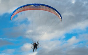 A paraglider cruises through a blue sky.