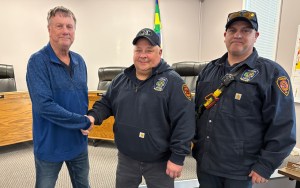 Two men in jackets shake hands with a third man.
