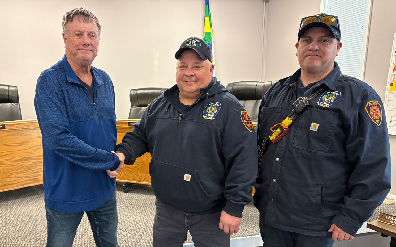 Two men in jackets shake hands with a third man.
