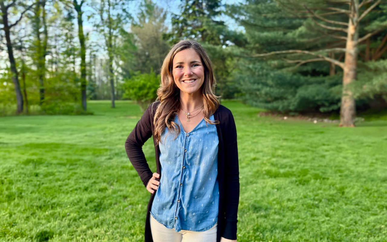 A woman standing in green grass and trees.
