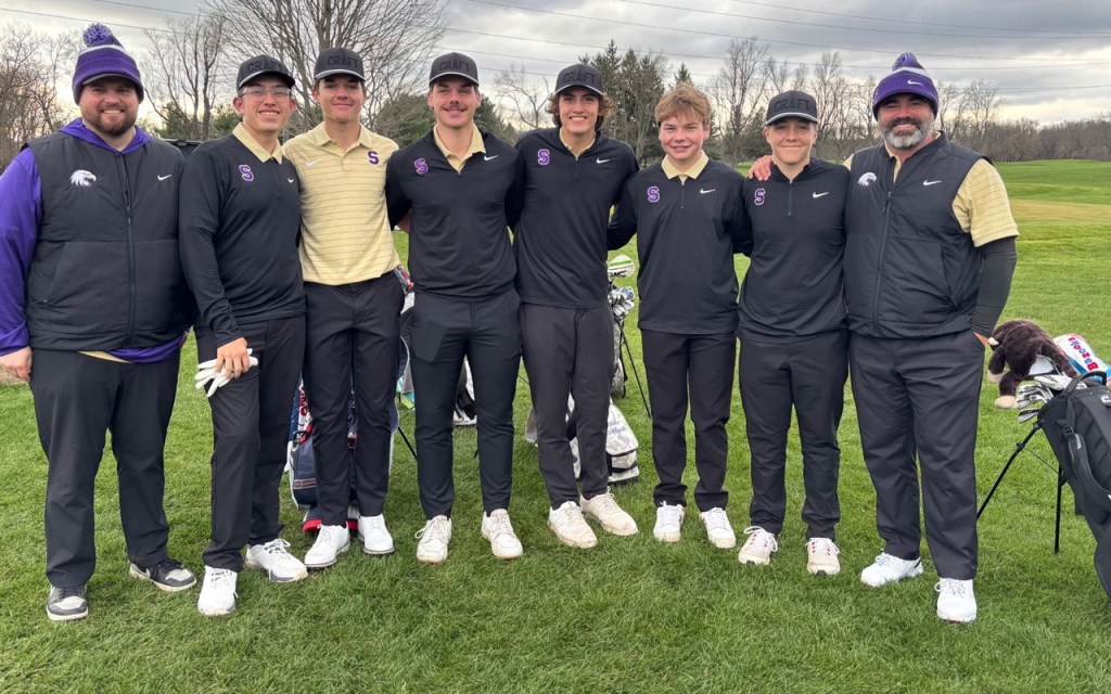 Golfers stand on the green in black, purple, and gold uniforms.