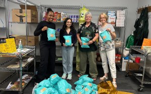 Four women stand in a stock room holding care packages.