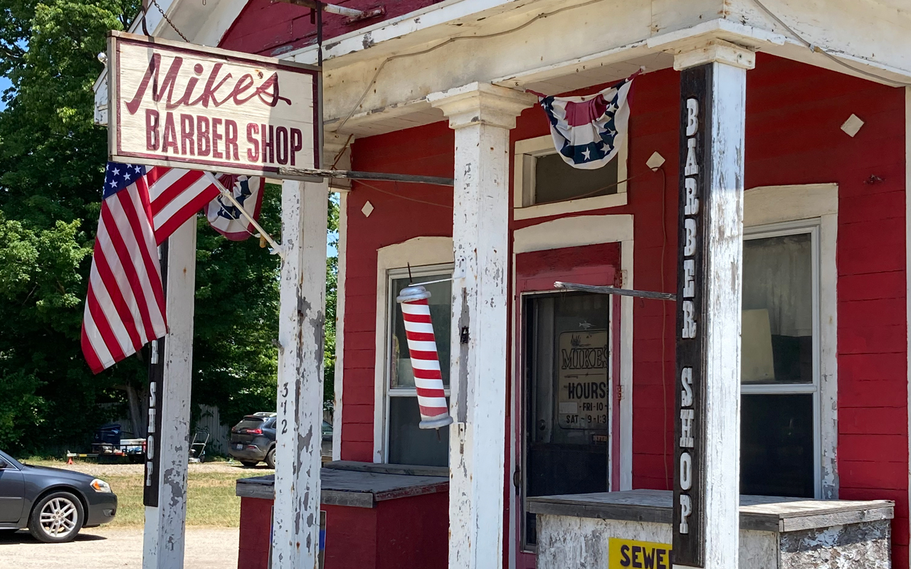 mikesbarbershop An old, red building with a US flag. The sign on it is labeled Mike's Barber Shop.
