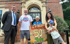 A multigenerational family holds a cardboard sign that reads "Delaware 50th State."