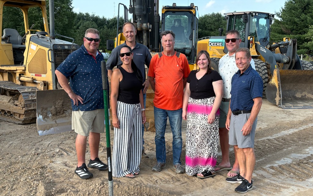 A group of men and women stand on the dirt by large construction machines.