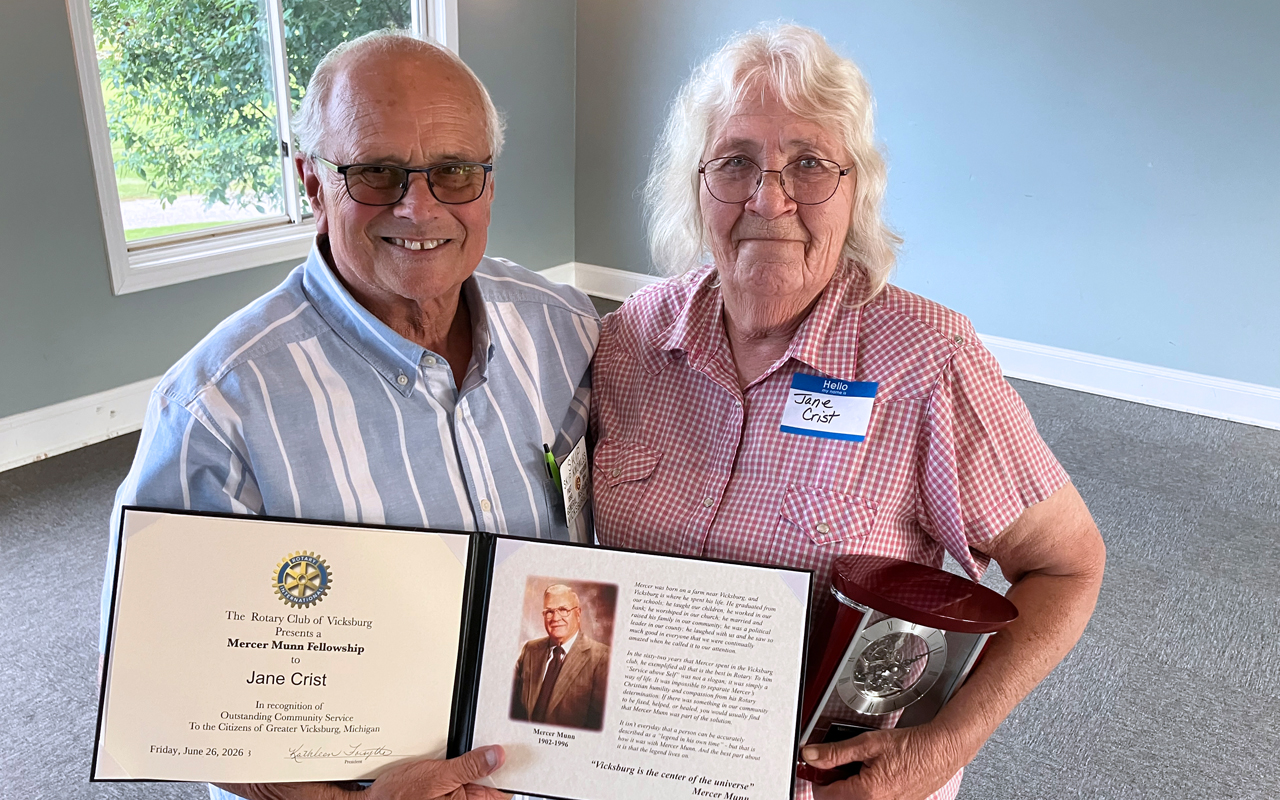 Two people with glasses hold up an award certificate and a clock.