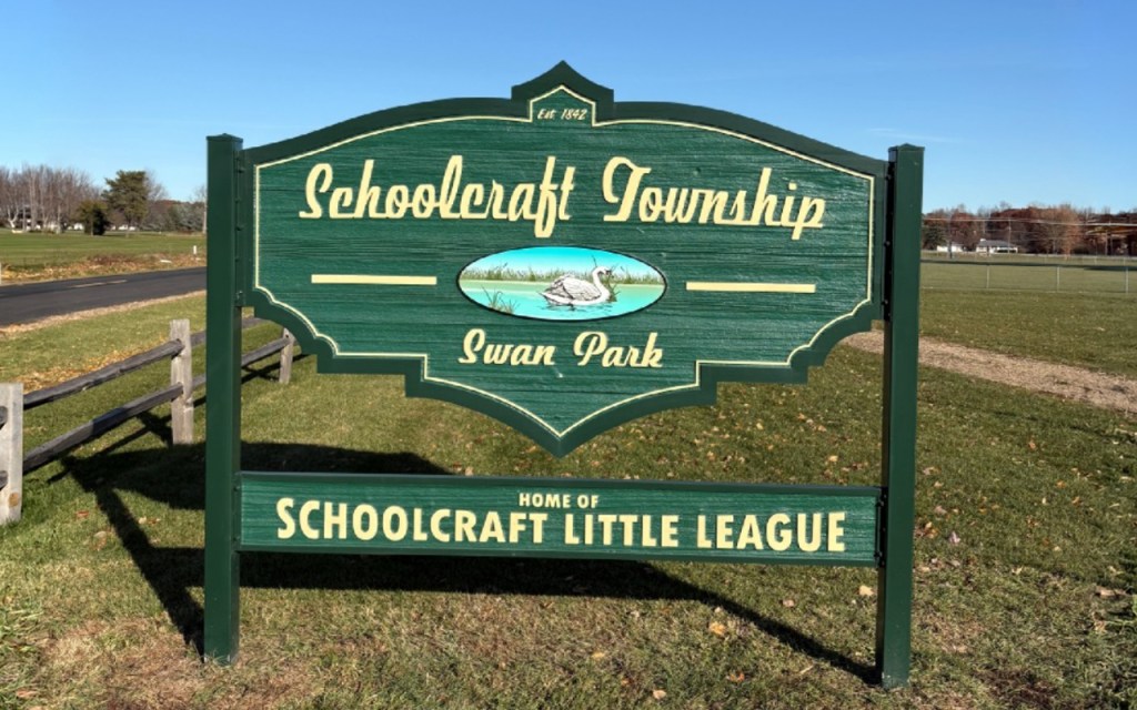 A green wooden sign reads "Schoolcraft Township - Swan Park." A lower portion of the same sign says "Home of Schoolcraft Little League."