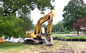 A yellow excavator breaks ground near a lake.