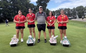 Four red-shirted golfers stand by their coach on the green.